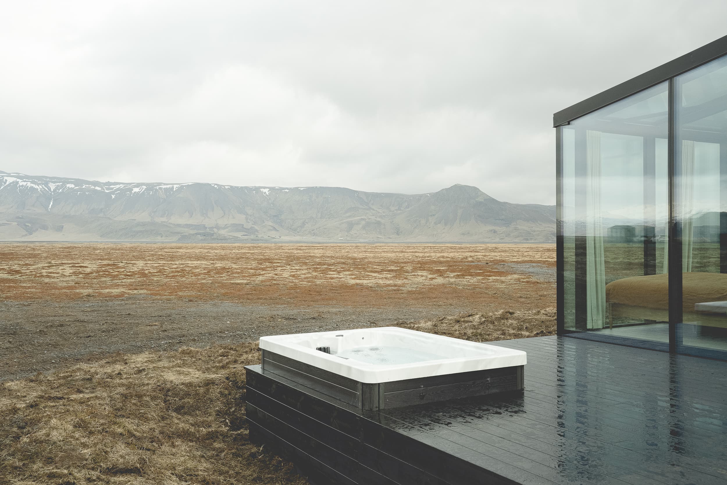 Outdoor hot tub on deck next to bedroom with glass walls at Rafter Seljalandsfoss Lilja, Hvolsvöllur