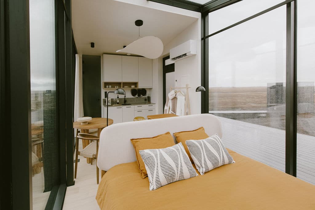 Modern bedroom with mustard bedding and panoramic windows showcasing Hvolsvöllur landscape at Rafter Seljalandsfoss Lilja