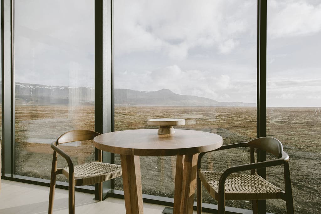 Dining area with round wooden table and chairs overlooking vast Icelandic plains at Rafter Seljalandsfoss Lilja in Hvolsvöllu