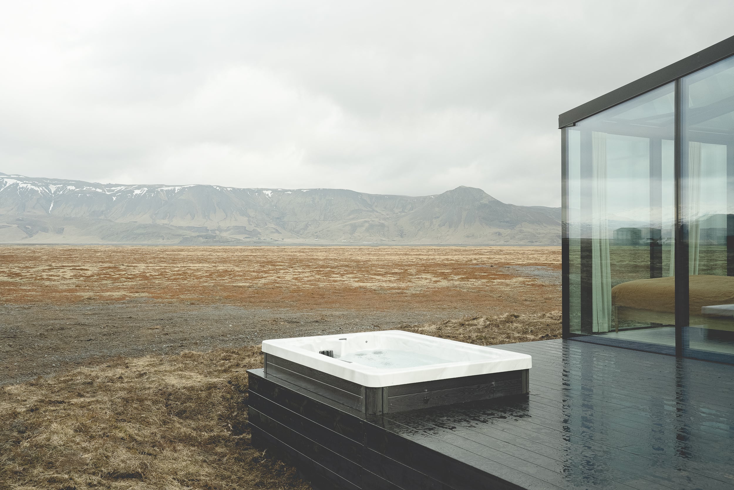 Outdoor hot tub on deck next to bedroom with glass walls at Rafter Seljalandsfoss Lilja, Hvolsvöllur