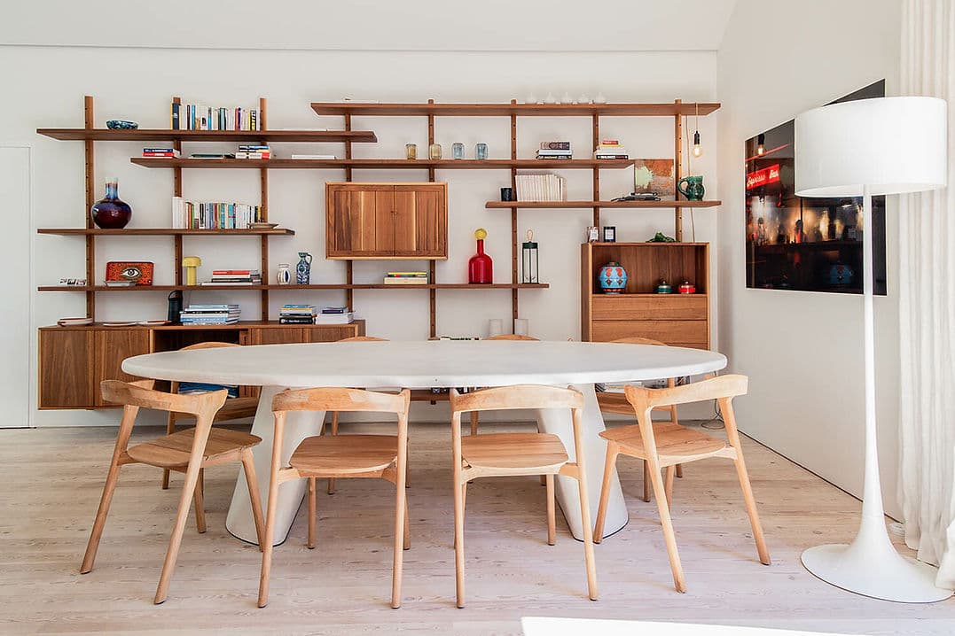 Dining area with oval table, wooden chairs, and wall shelving at Rafter Melides Atlantica in Melides, Portugal