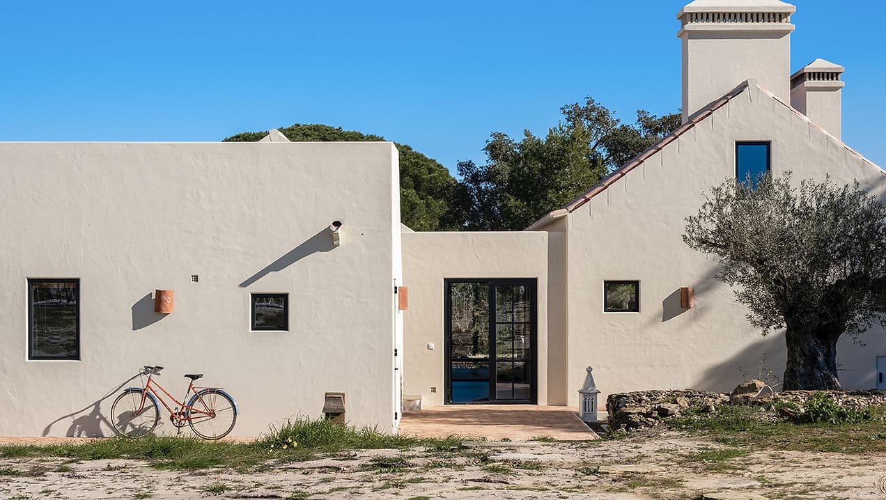 Exterior view of Rafter Melides Serena with white walls, black windows, and a vintage bicycle in Melides, Portugal