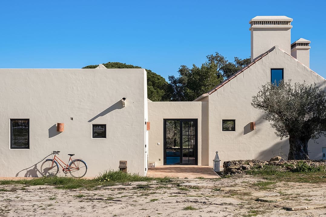 Exterior view of Rafter Melides Serena with white walls, black windows, and a vintage bicycle in Melides, Portugal