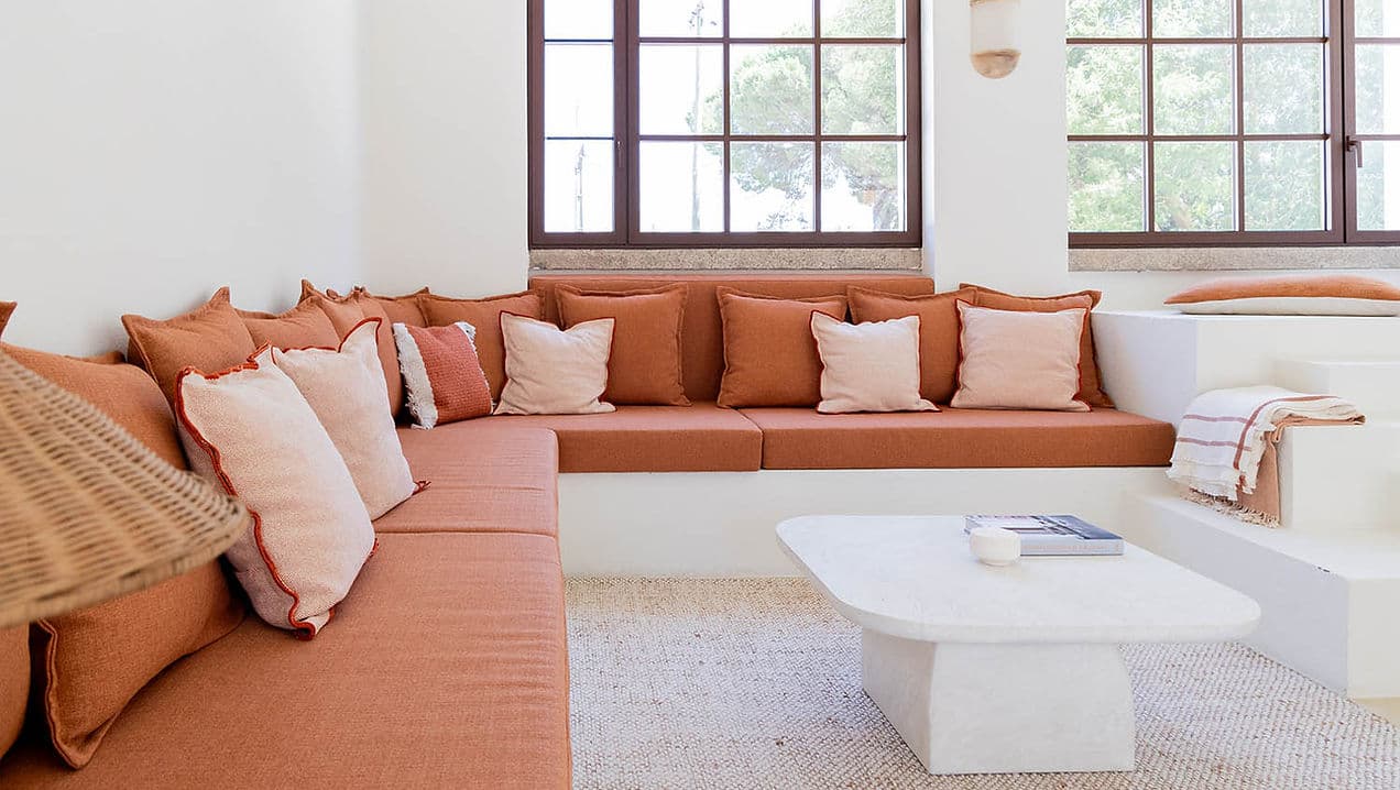 Built-in corner sofa with terracotta cushions and large windows in Rafter Carvalhal Bicas living room, Carvalhal