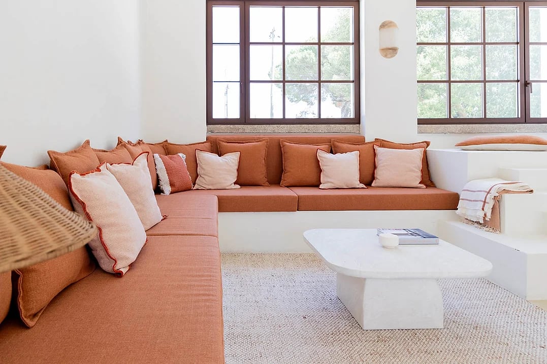 Built-in corner sofa with terracotta cushions and large windows in Rafter Carvalhal Bicas living room, Carvalhal