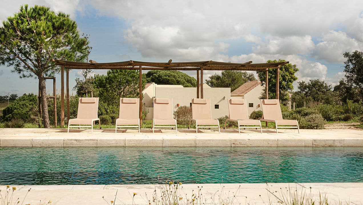 Outdoor pool with six beige loungers under wooden pergola at Rafter Melides Serena in Melides, Portugal