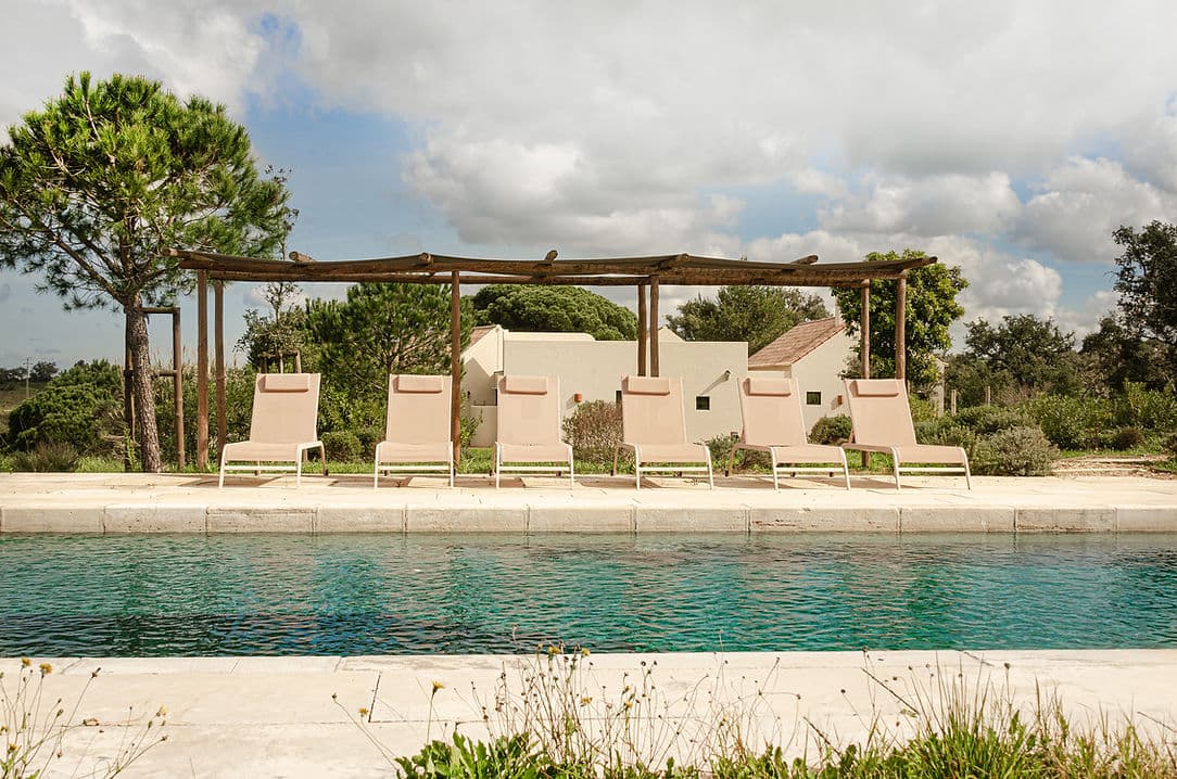 Outdoor pool with six beige loungers under wooden pergola at Rafter Melides Serena in Melides, Portugal