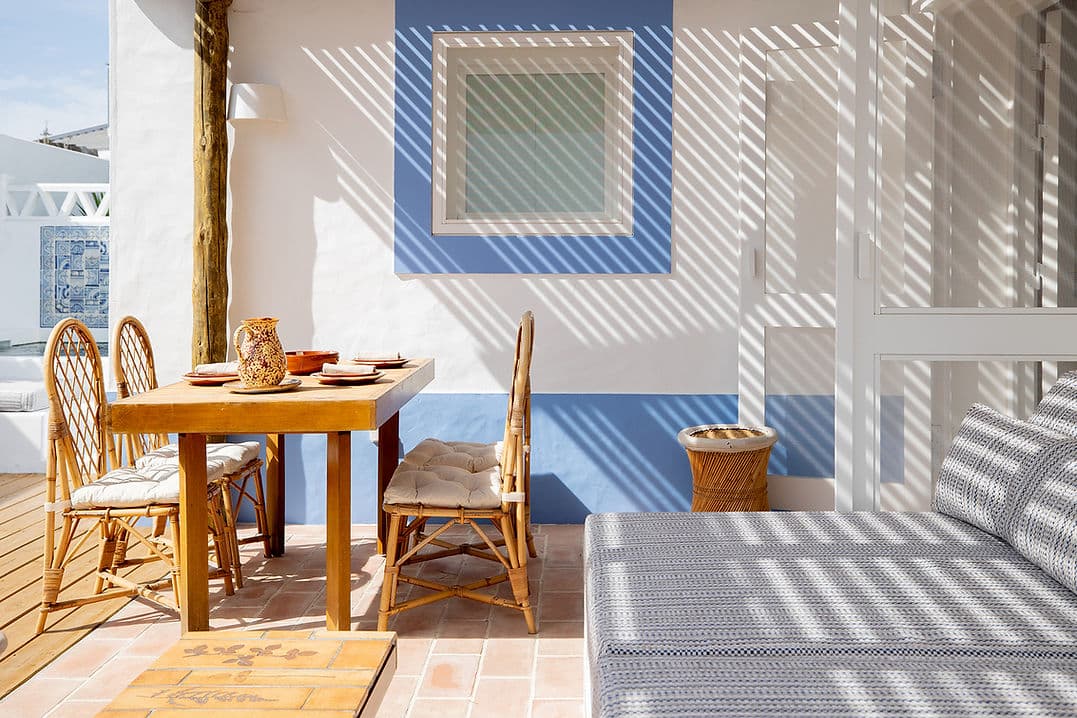 Outdoor dining area with rattan chairs and shaded seating at Casa Mounette in Portugal