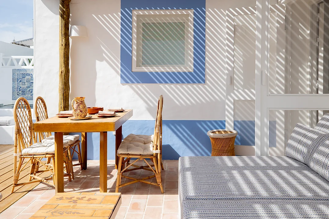 Outdoor dining area with rattan chairs and shaded seating at Casa Mounette in Portugal