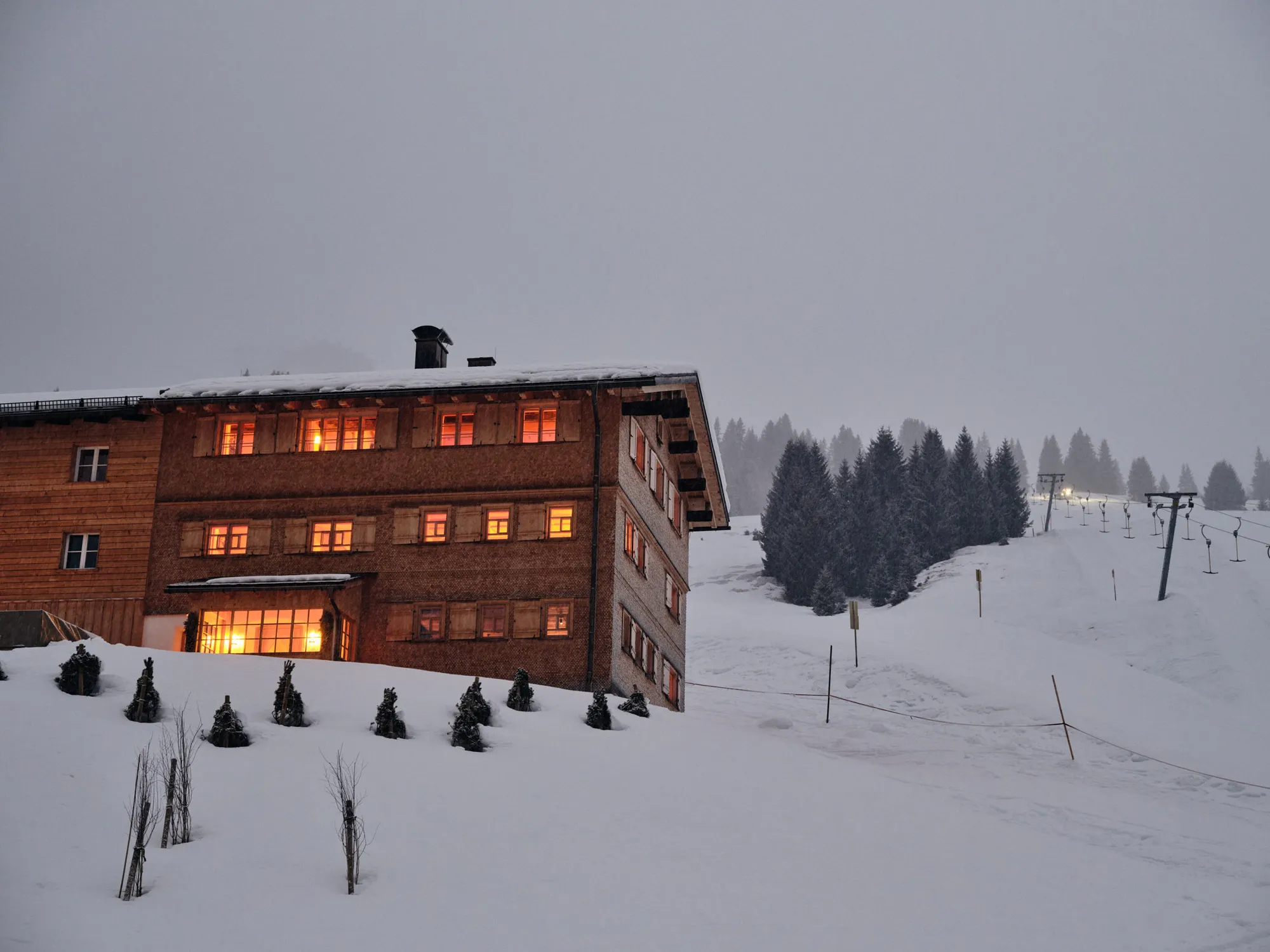 Rafter Lech chalet exterior at dusk with snowy ski slope and pine tree view in Lech, Austria