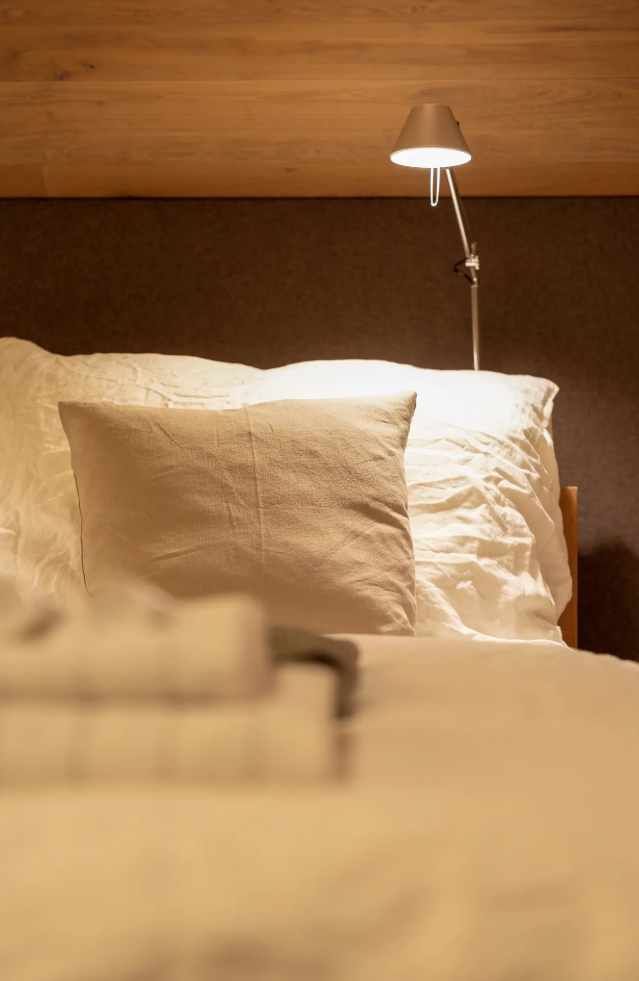Minimalist bedroom detail with reading lamp and linens at Rafter Bramberg in Bramberg am Wildkogel, Austria