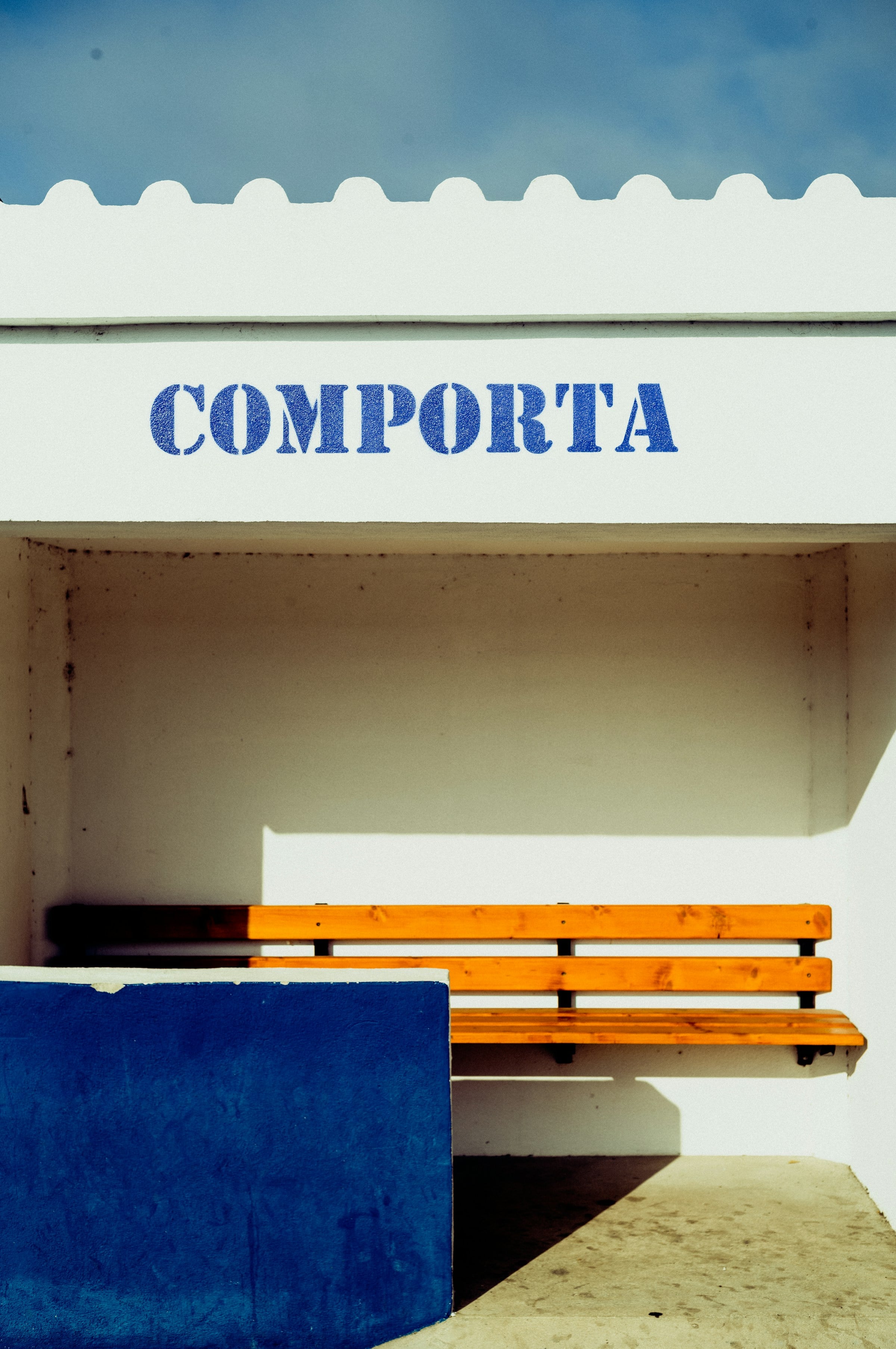 Whitewashed building with a blue wall and a bench and Comporta written on the ceiling in Comporta village