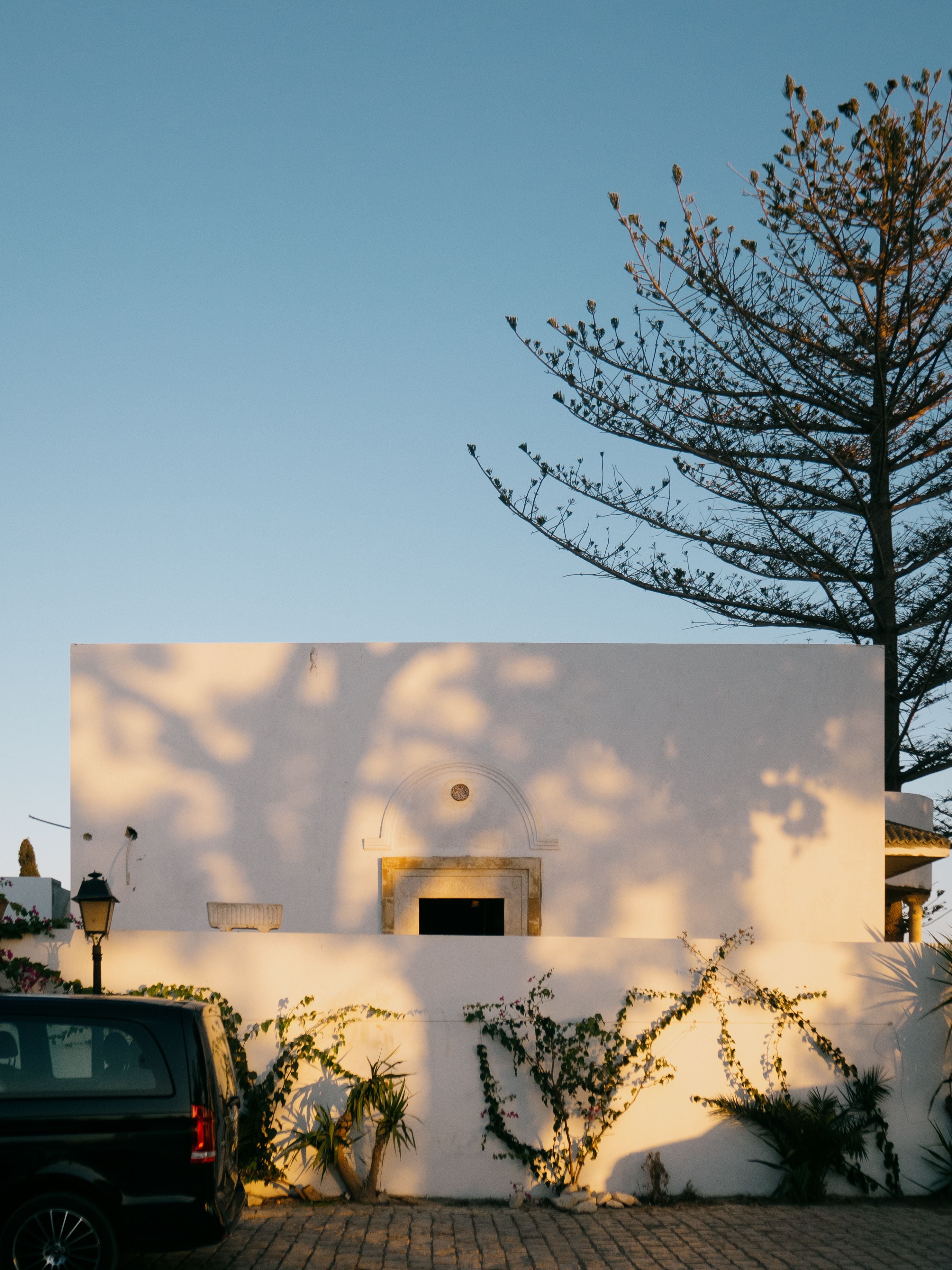 A typical Portuguese house in the evening sun with shadows from a tree on it and a car parked in front